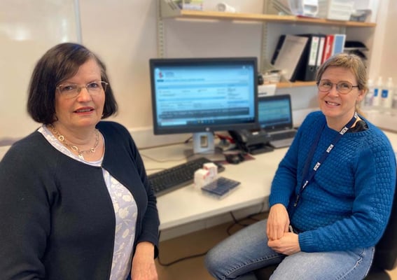 To ansatte i Kristiansand kommune sitter ved et skrivebord foran en dataskjerm som viser kjernejournal.