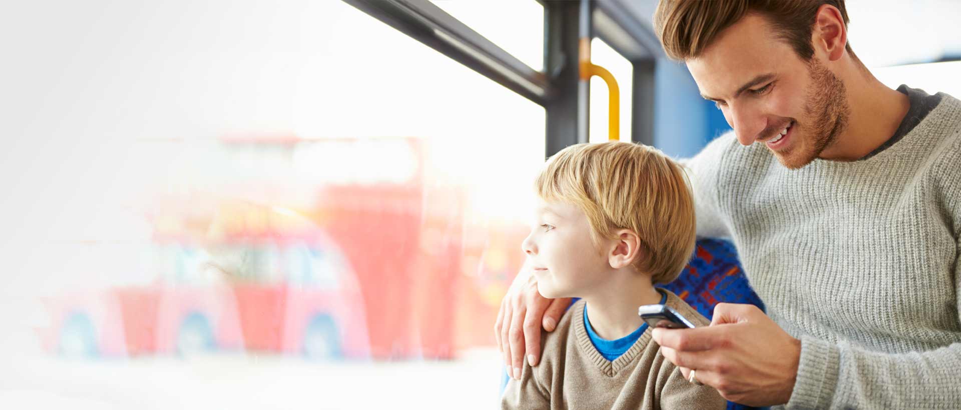 En far og hans sønn sitter sammen, hvor faren smiler ned på sin smarttelefon, sannsynligvis ved bruk av Min Skole appen. Bildet symboliserer en intuitiv dialog mellom skole og hjem, muliggjort gjennom skole-appen for ansatte.