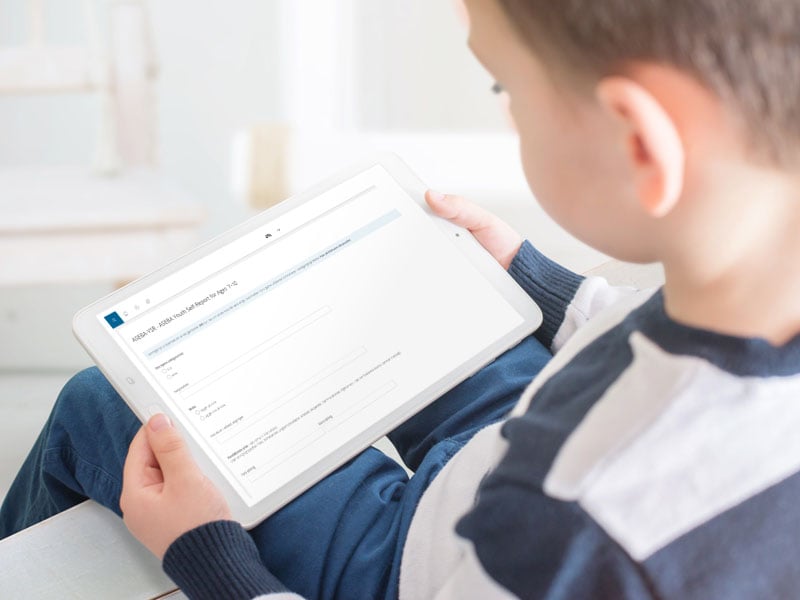 En ung person ser på et nettbrett som viser et digitalt ASEBA-skjema for enkel kartlegging.
