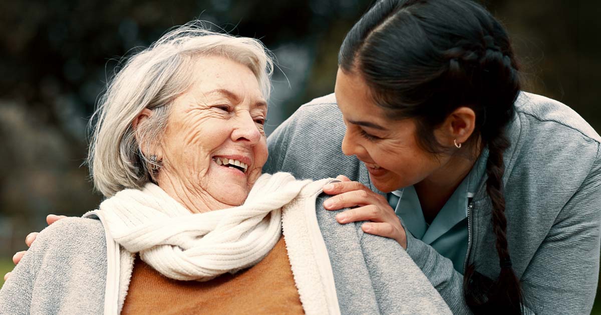 En smilende eldre kvinne får omsorg av en helsearbeider, som illustrerer trygg oppfølging med EPJ i den kommunale helsetjenesten.
