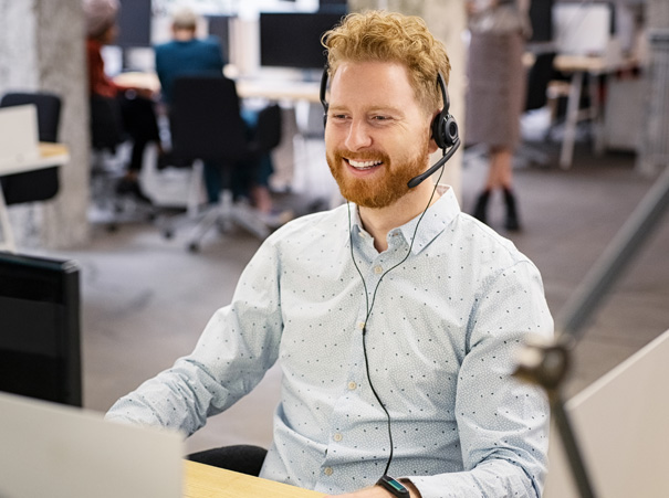 Smilende kundeservicemedarbeider med headset som tilbyr support fra Flyt i et moderne kontormiljø.