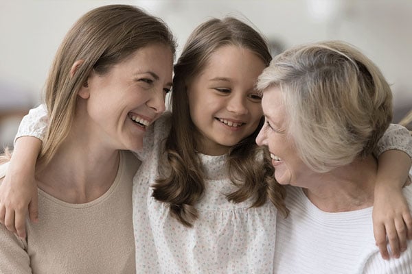 Tre generasjoner kvinner – en bestemor, en mor og et barn – smiler og holder rundt hverandre. Som et visuelt symbol på tverrfaglig samarbeid.